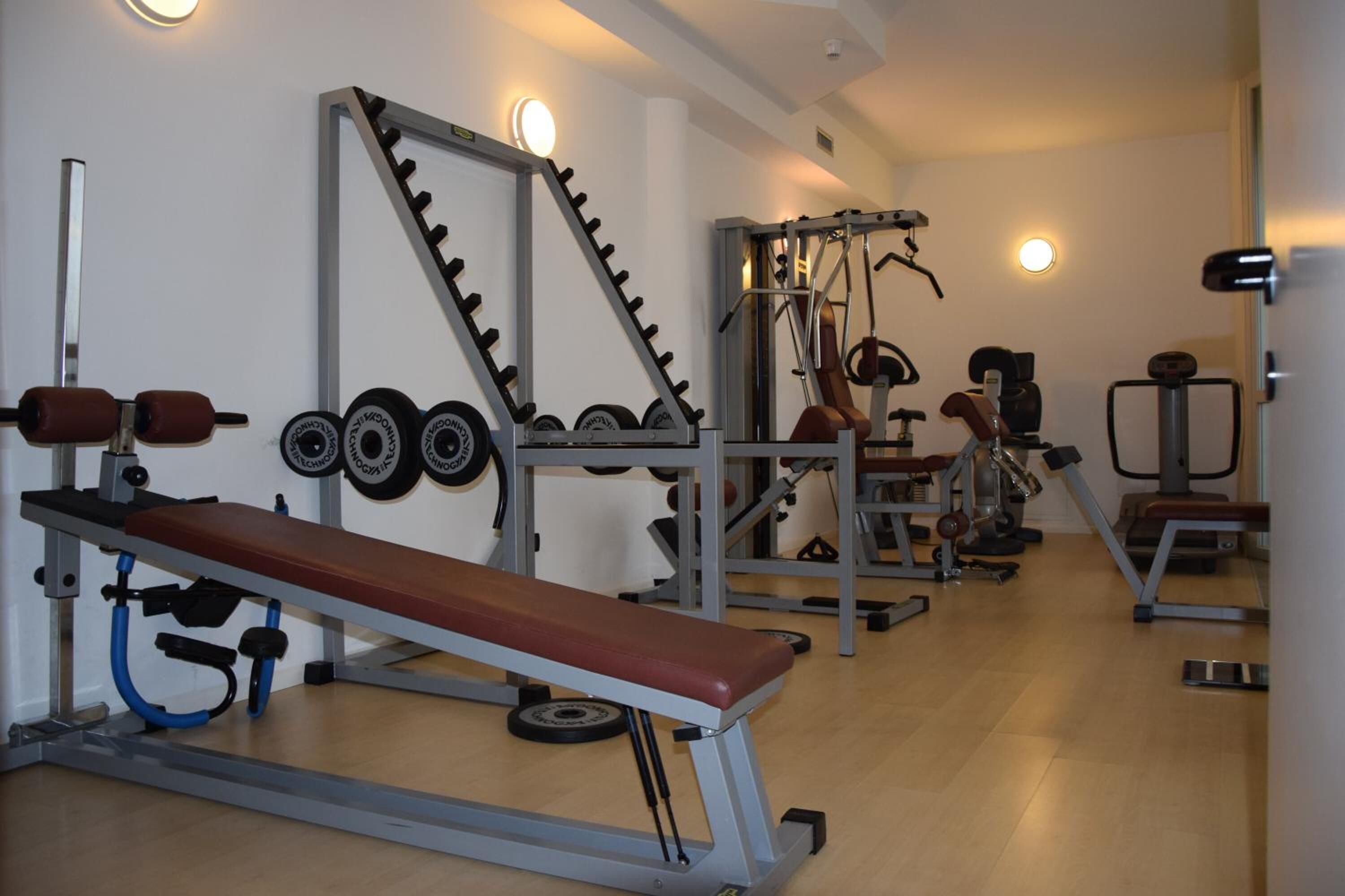 A gym with a bench press, weight plates, and various exercise machines.