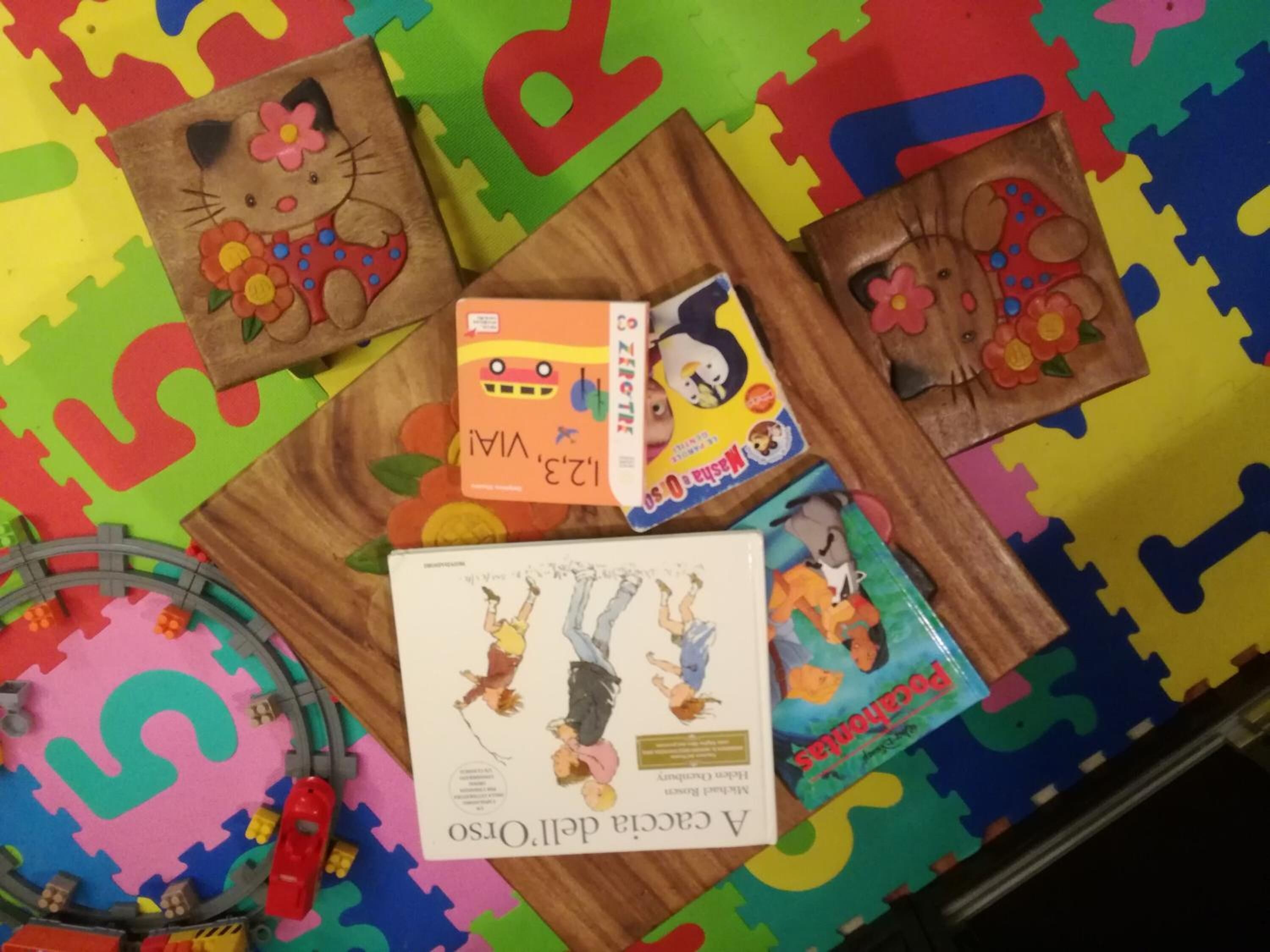 A colorful play mat with puzzle pieces, a Hello Kitty-themed mat, and a book titled 'A Cacique Del Orito'.