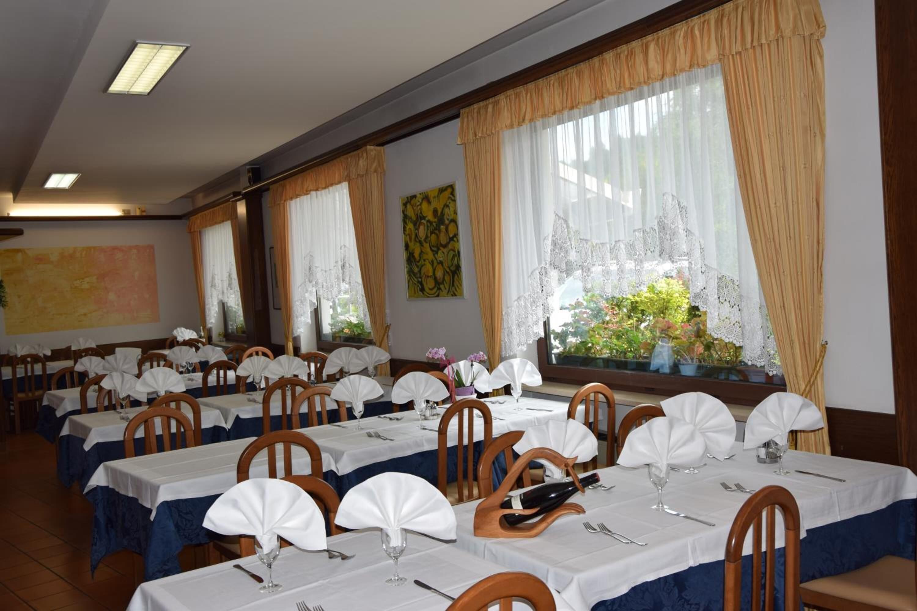 A dining area with multiple tables set for service, each with white tablecloths and wooden chairs.