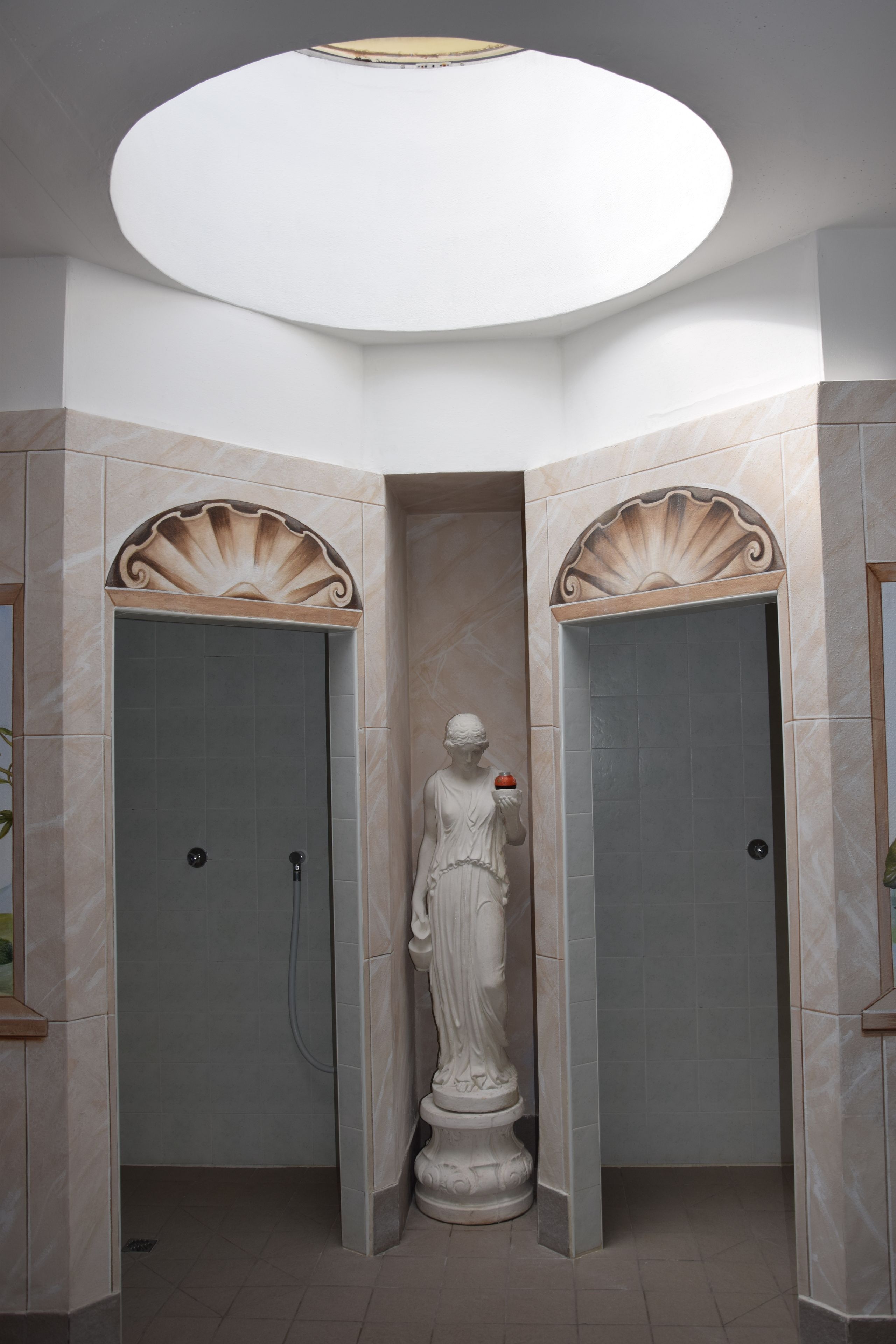 A bathroom with a statue, two shower stalls, and a skylight.