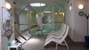 A spa area with reclining chairs, a small table with amenities, and a glass-enclosed pool. - Hotel Olimpic (Baselga di Pine)