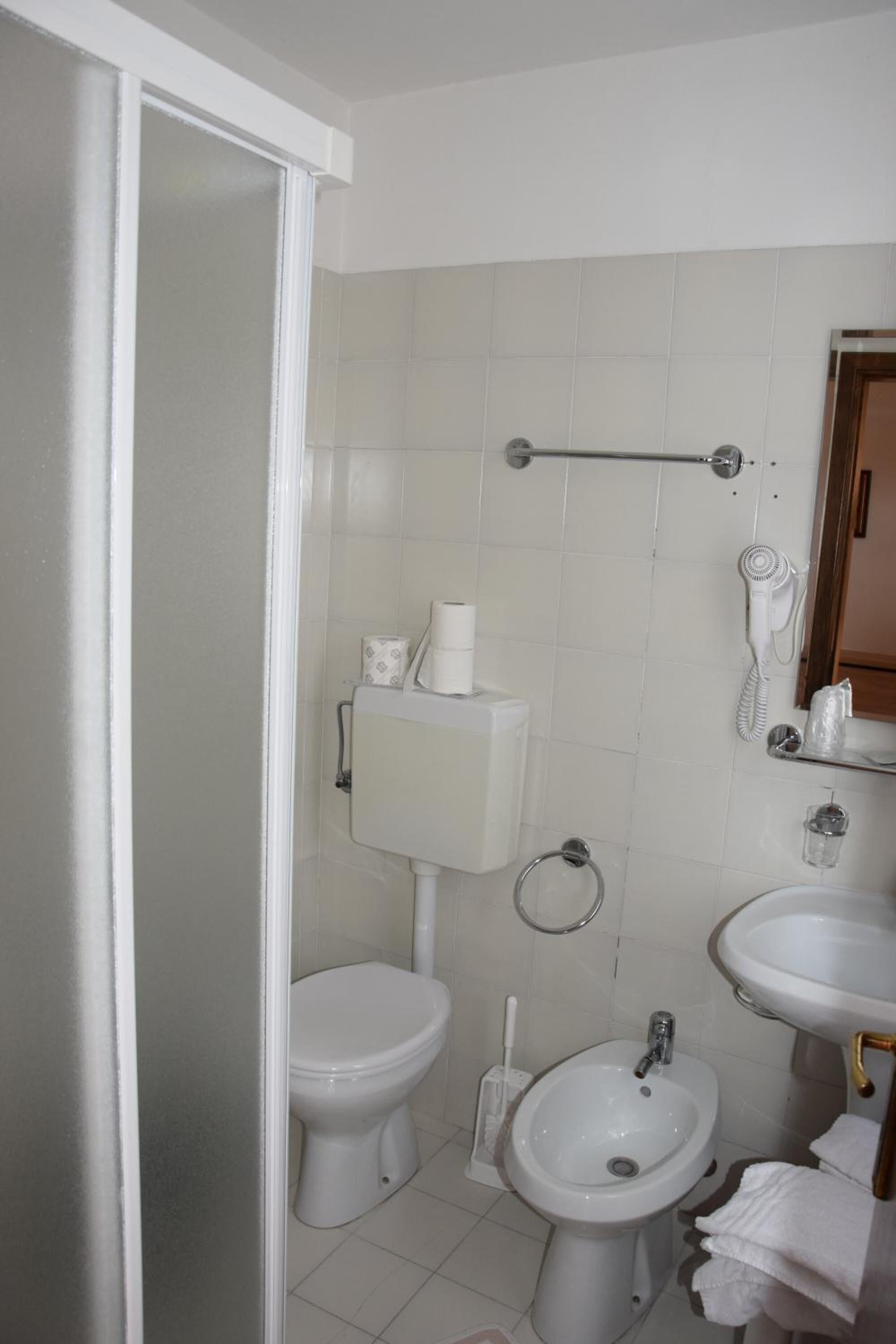 Et badeværelse med toilet, bidet, vask og et håndklædetørrestativ.