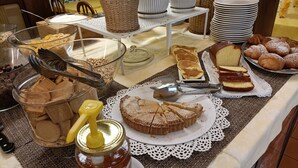 A buffet table with various food items including pastries, bread, and a jar of honey. - Hotel Olimpic (Baselga di Pine)