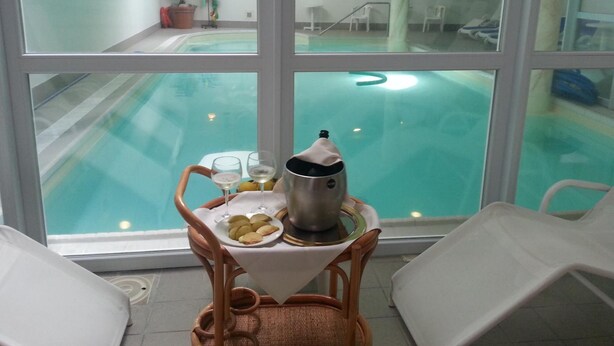 A poolside area with a table set for two, a potted plant, and a view of the pool. - Hotel Olimpic (Baselga di Pine)