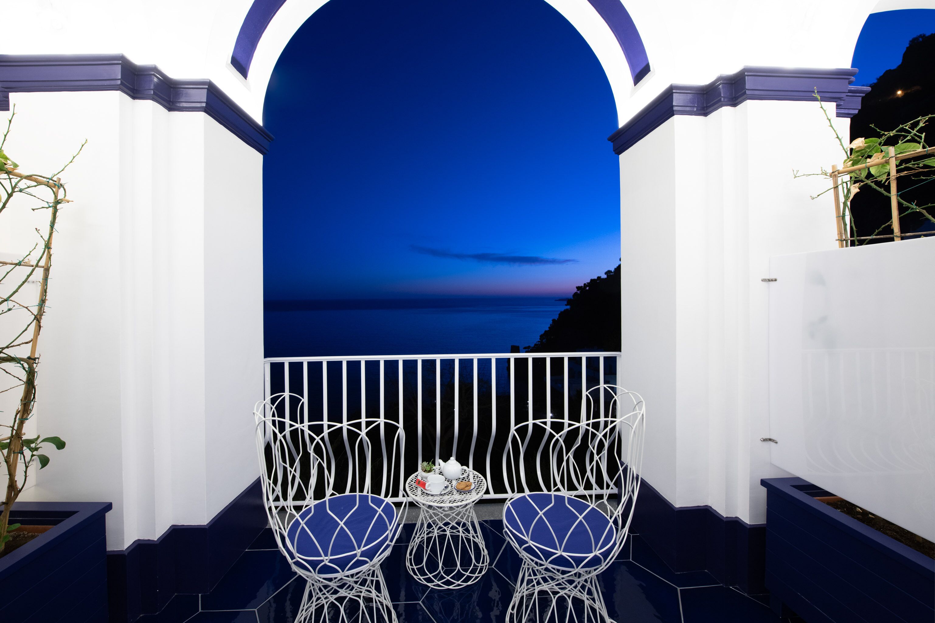 A balcony with two white wire chairs and a small table with a teapot and cups.