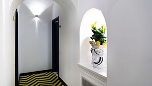 Un pasillo con piso de diseño a cuadros negros y amarillos, pared blanca y una puerta blanca con una lámpara arriba.
