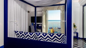 Un dormitorio con vista al mar, una cama con almohadones estampados, un televisor y una mesita con un florero.