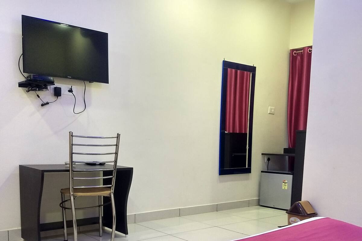 A hotel room with a bed, a desk, a chair, a television mounted on the wall, and a window with curtains.