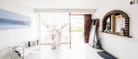 A bright, modern interior with a tiled floor, a white bench, a potted plant, and a view of the outdoors.