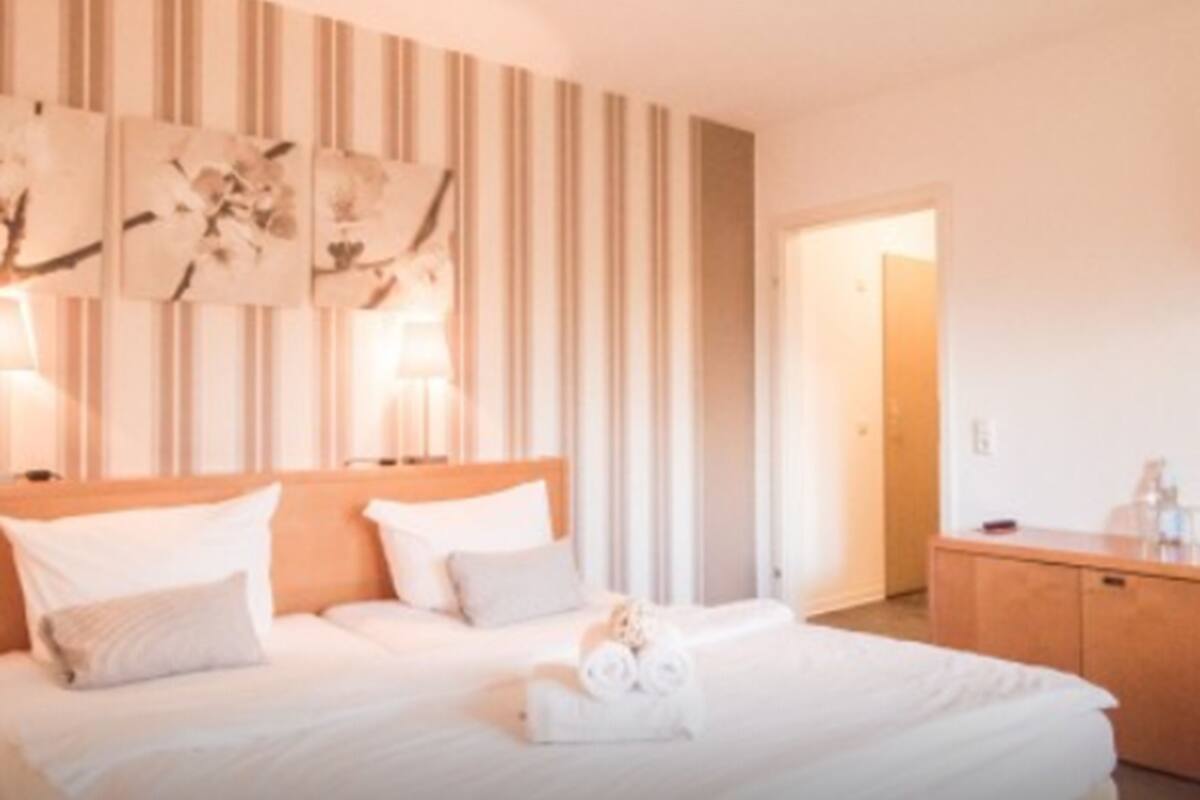A hotel room with a bed, a wooden headboard, a nightstand, and a door leading to another room.