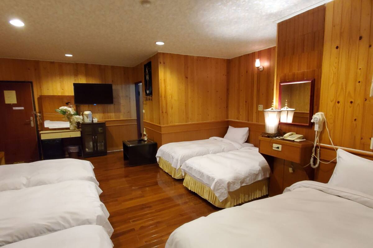 Habitación de hotel con paneles de madera, dos camas, un escritorio con silla, televisión, teléfono y espejo.