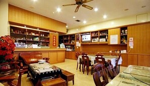 A traditional Japanese-style room with wooden paneling, a ceiling fan, a television, and a dining area with tables and chairs.