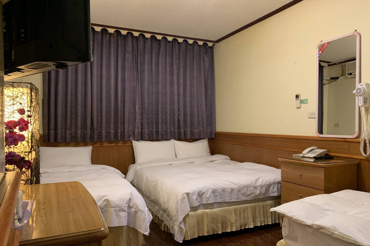 Habitación de hotel con dos camas, un aparador de madera, una mesita de noche, un espejo y un teléfono.