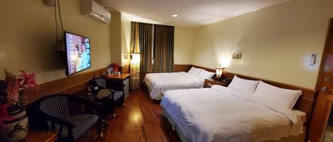 A hotel room with two beds, a TV, a desk with a chair, a vase with flowers, and a lamp.