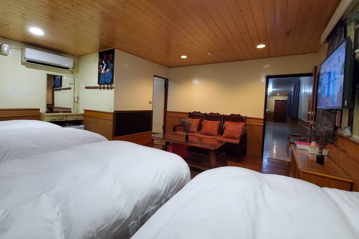 Habitación de hotel con dos camas, un sofá, un televisor y un aire acondicionado.