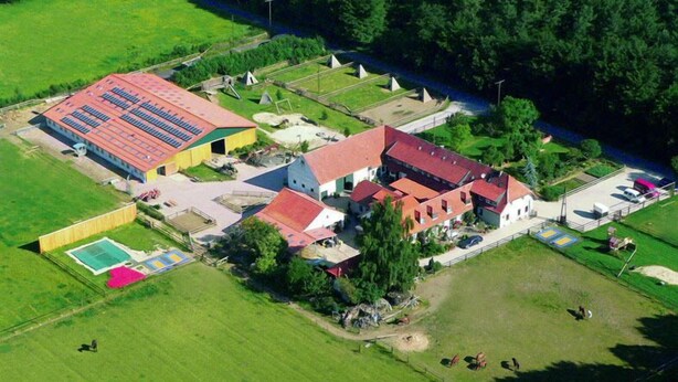 Vista aérea de una propiedad rural con un granero, un edificio más pequeño y un área cercada con caballos.
