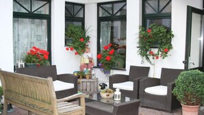Un espacio al aire libre con mobiliario de mimbre, una mesa con superficie de vidrio y plantas en macetas.