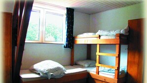Una habitación pequeña y funcional con una cama litera y una cama individual, una ventana con cortinas y una puerta.