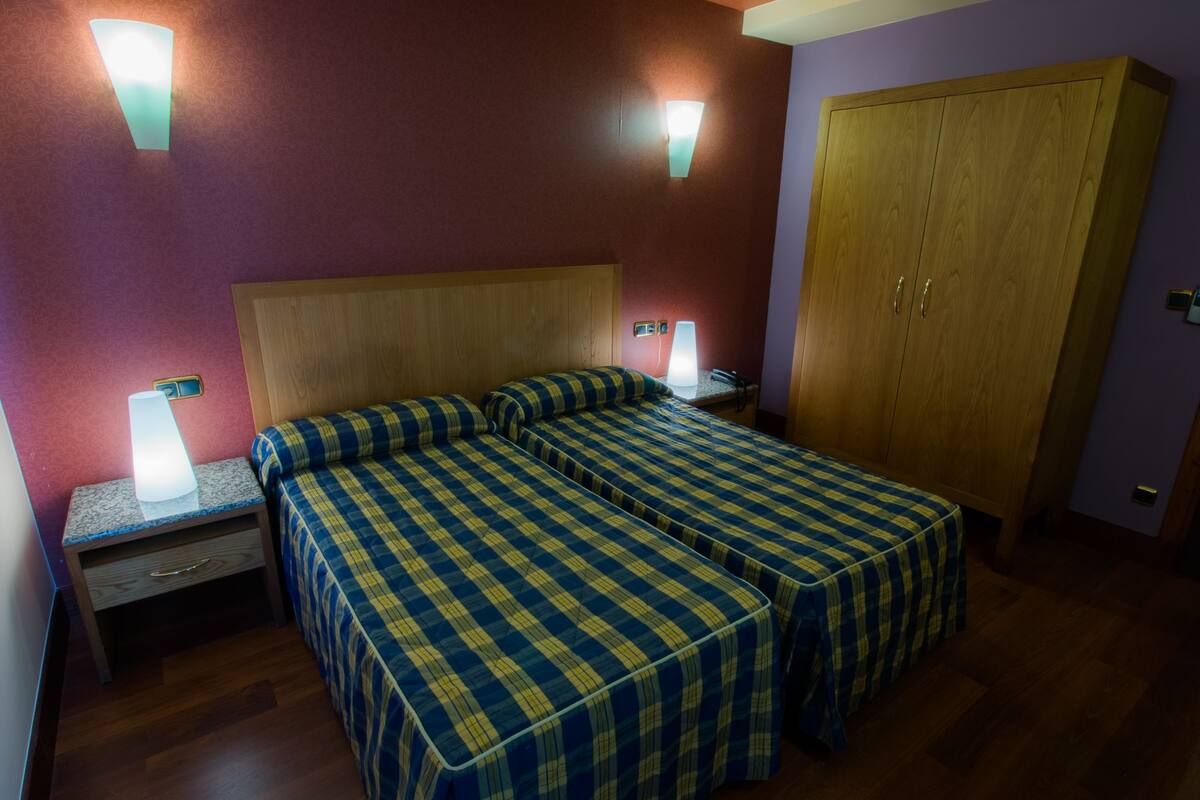 Una habitación con una cama doble, dos lámparas de noche, un armario de madera y una mesita de noche con lámpara.