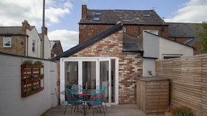 A patio with a table and chairs, a wooden fence, and a brick wall. - The Old Post Office - Bright & Modern 4bdr Townhouse With Private Garden (Oxford)