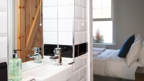 A bathroom with a white tiled wall, a sink with two faucets, and a mirror. - The Old Post Office - Bright & Modern 4bdr Townhouse With Private Garden (Oxford)