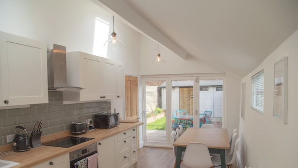 A modern kitchen with white cabinets, a wooden countertop, and a dining area with a table and chairs. - The Old Post Office - Bright & Modern 4bdr Townhouse With Private Garden (Oxford)