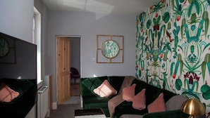 A living room with a green sofa, a small table, and a patterned wallpaper. - The Old Post Office - Bright & Modern 4bdr Townhouse With Private Garden (Oxford)