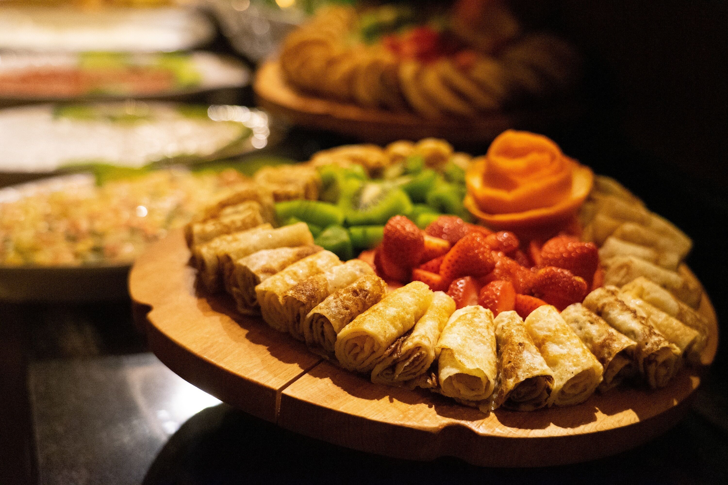 A wooden board with rolled pastries and fresh strawberries.