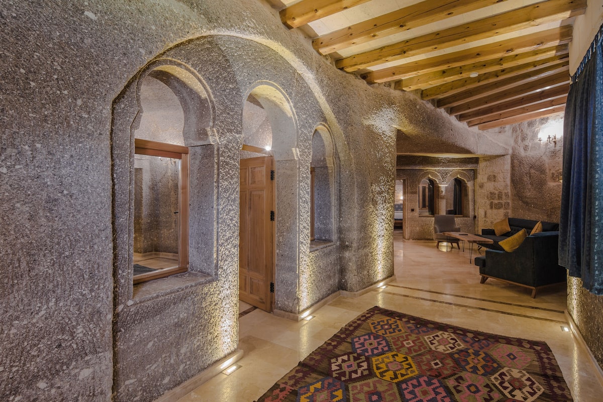 Interior de paredes de piedra con vigas de madera, un tapiz estampado y una zona de estar.