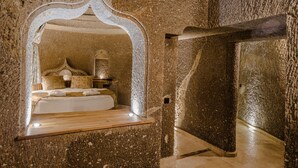 Una habitación con paredes de piedra, una cama, una mesita de noche y un espejo decorativo.