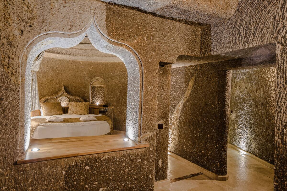 Una habitación con paredes de piedra, una cama, una mesita de noche y un espejo decorativo.
