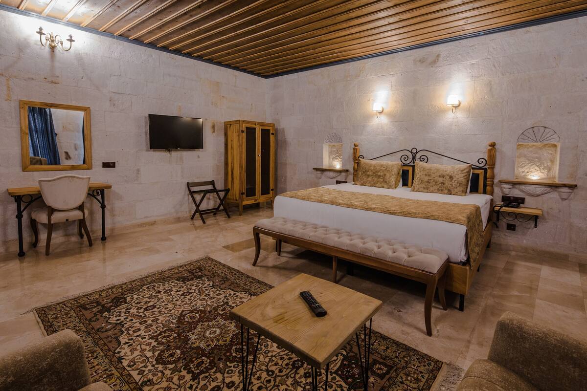 Un dormitorio con una cama grande, un banco de madera, una mesita, una silla, un televisor y apliques de pared.