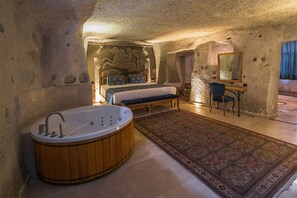 A bedroom with a large bathtub, a bed, a desk with a chair, and a patterned rug.