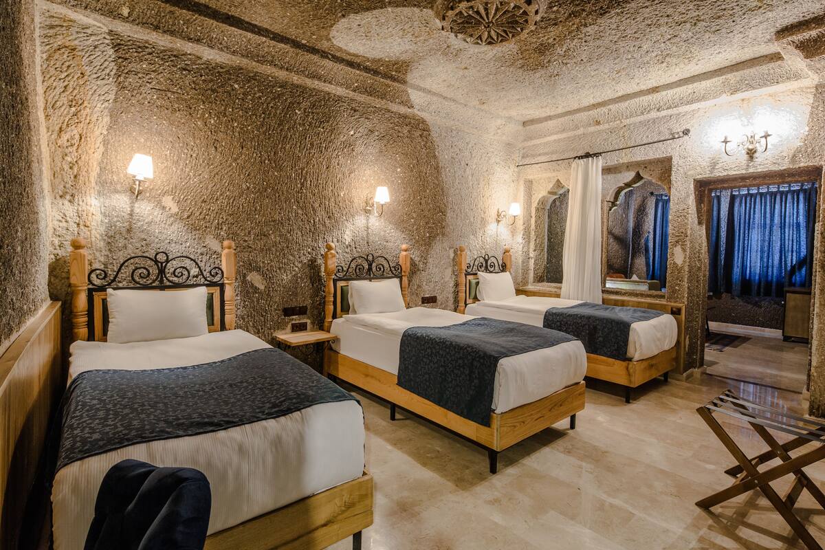 Una habitación con tres camas de madera, paredes de piedra y una araña.