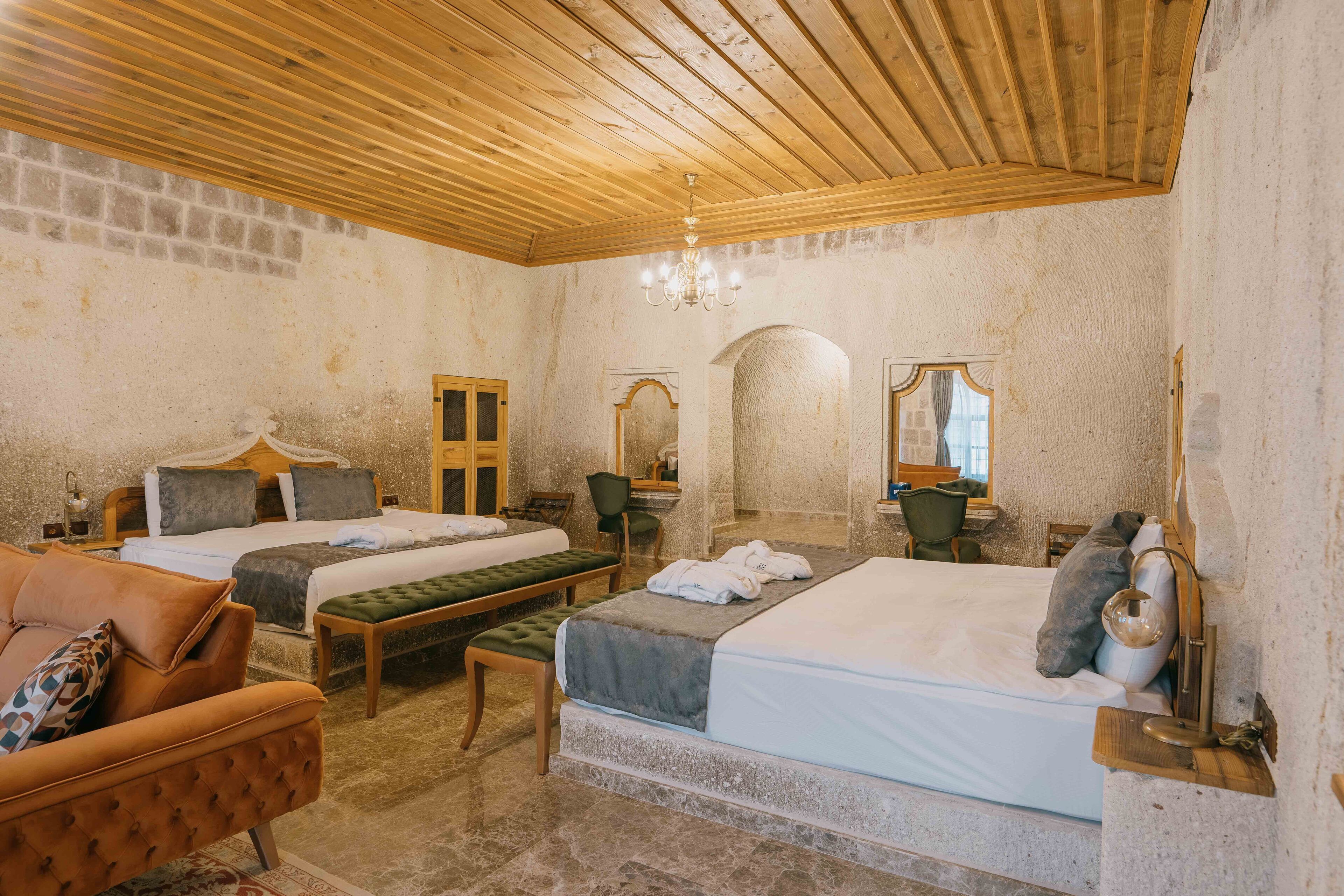 Une chambre avec deux lits, un plafond en bois, des murs en pierre, un lustre et une petite table avec des chaises.