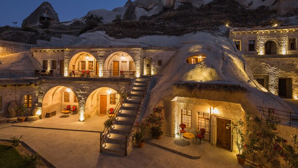 Un hotel con arquitectura singular tipo cueva, con varios niveles, una escalera central y zonas de estar al aire libre.