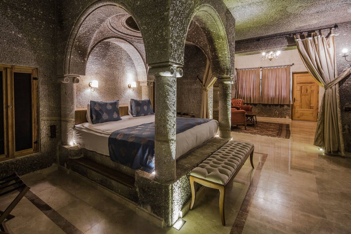 Un dormitorio con paredes de piedra, una cama con dosel, un banco y una araña.