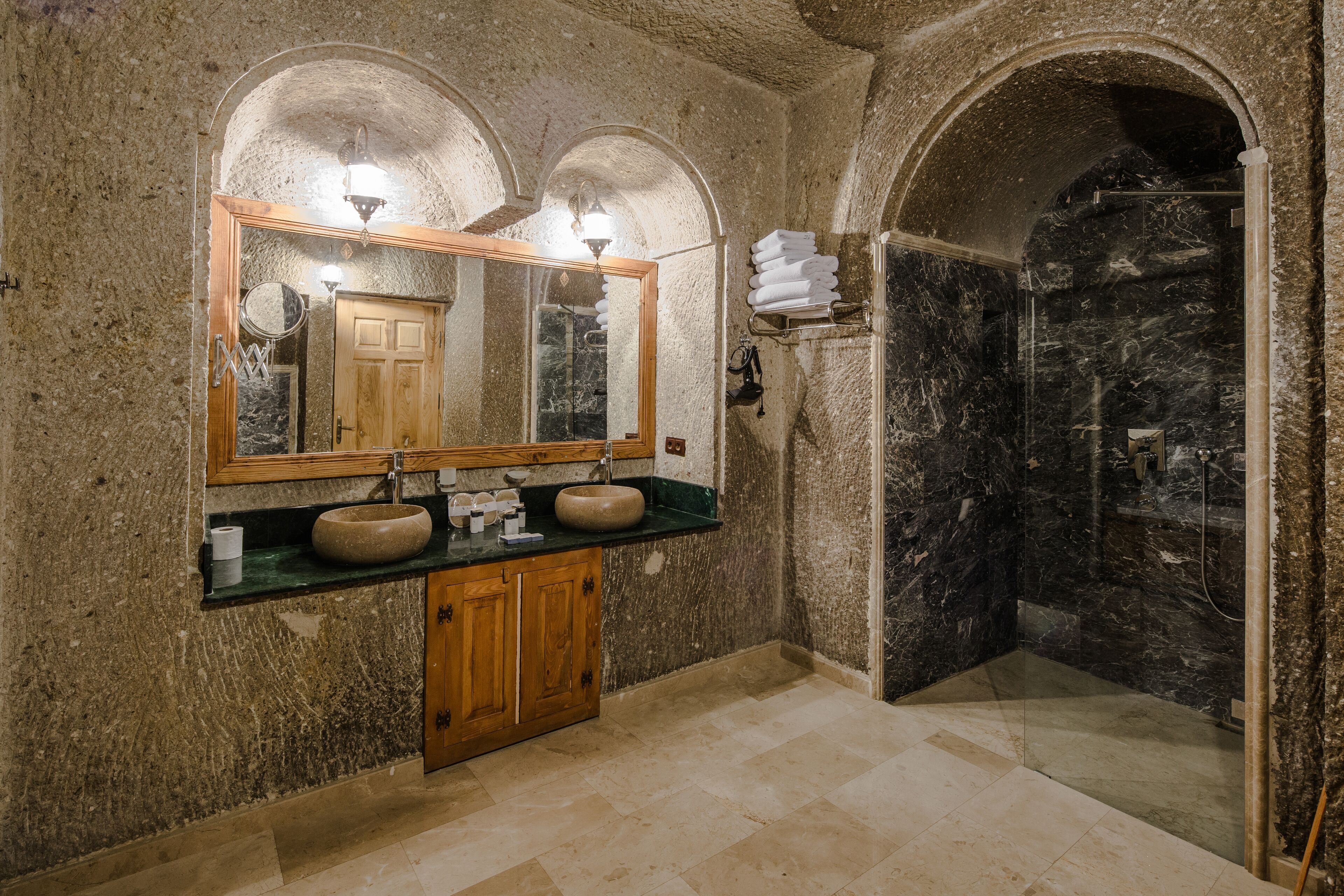 A bathroom with a stone wall, wooden cabinets, a sink, a mirror, and a shower area.