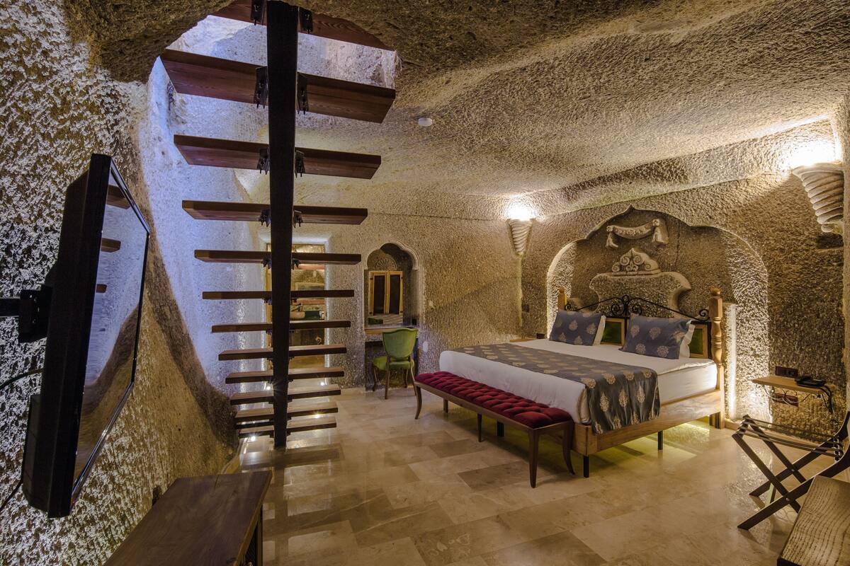 Una habitación con cama, una banca, una silla, un escritorio y una escalera.