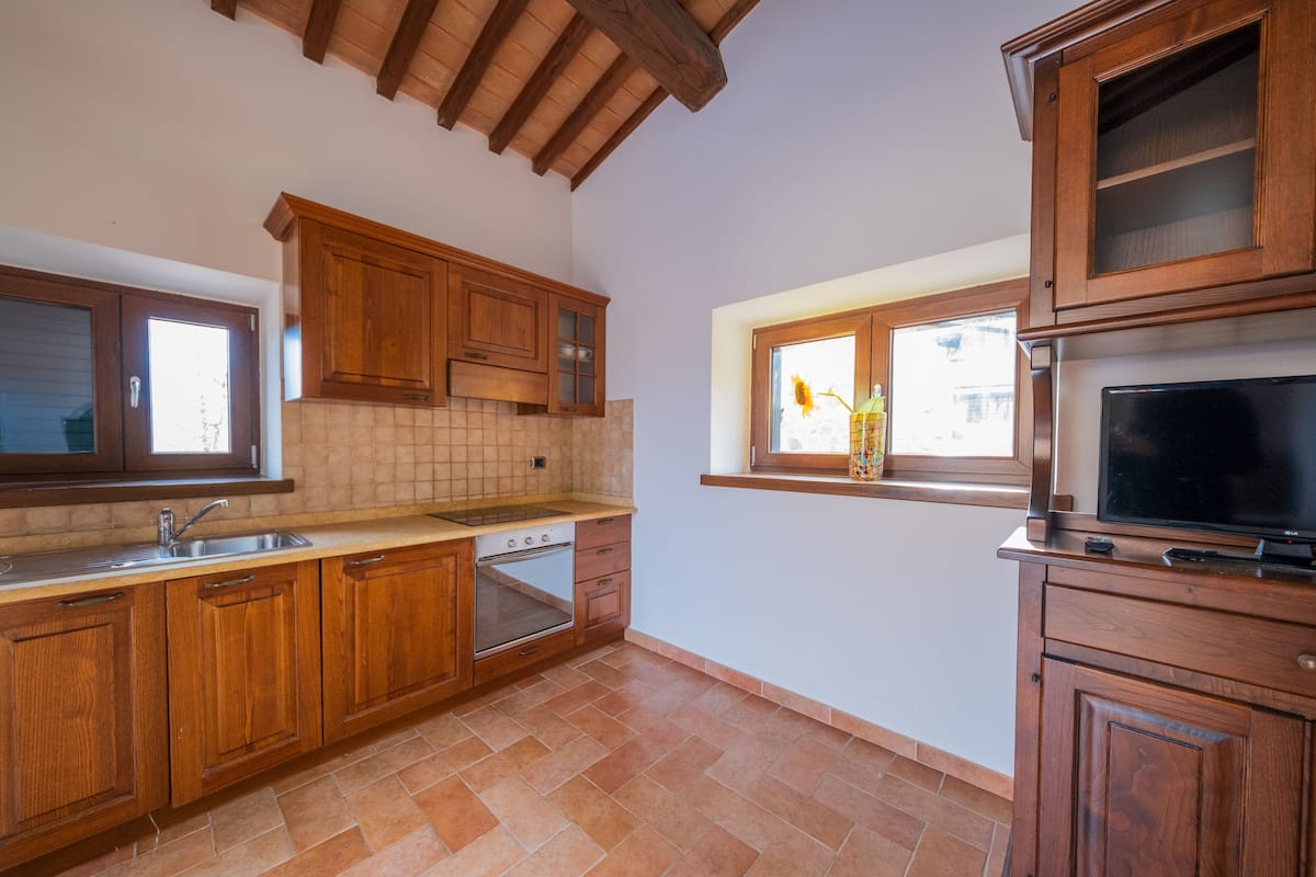 Una cocina con armarios de madera, horno empotrado y una ventana con un jarrón de flores.