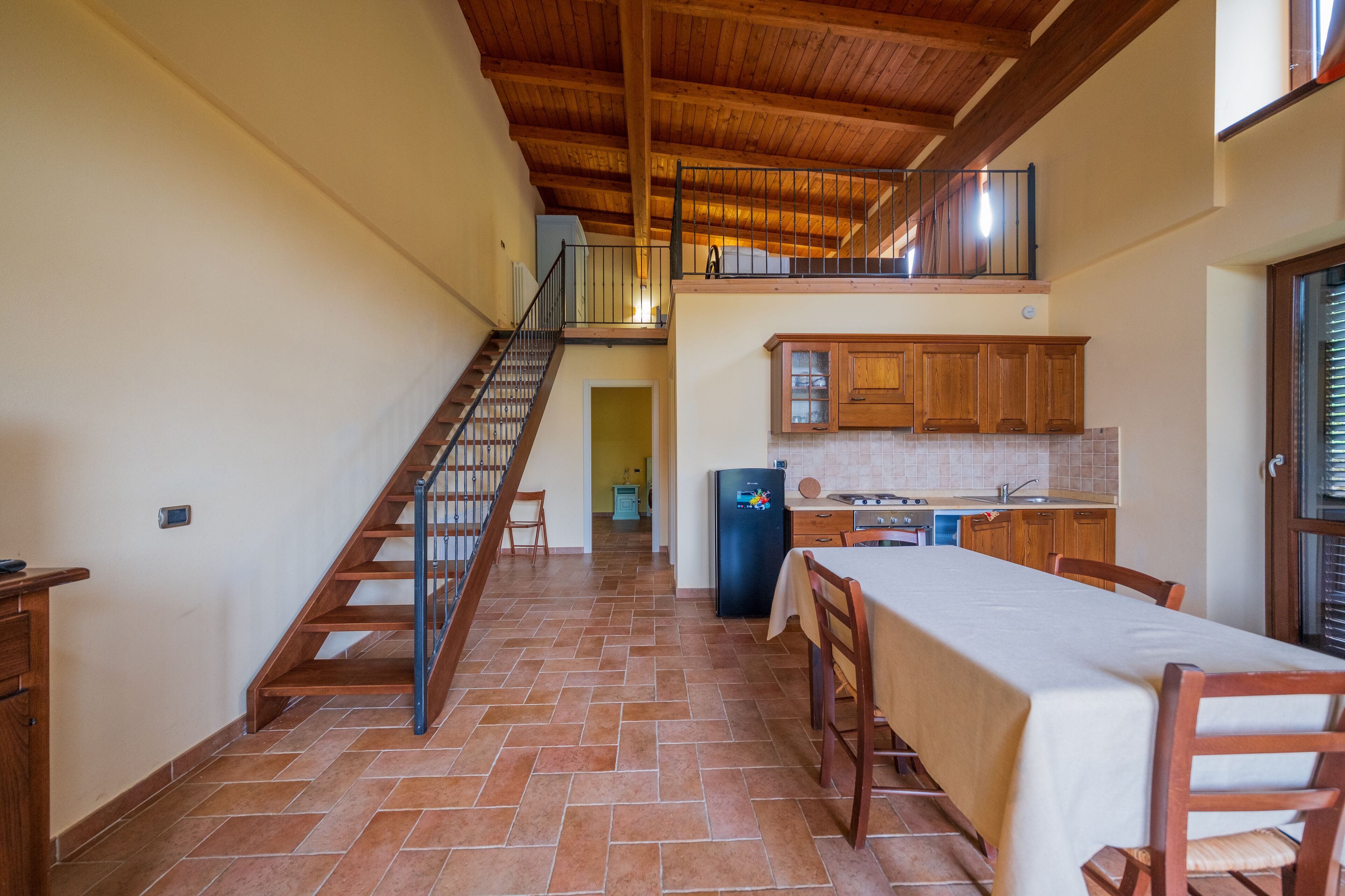 A spacious kitchen with wooden cabinets, a dining table, and a staircase leading to an upper level.