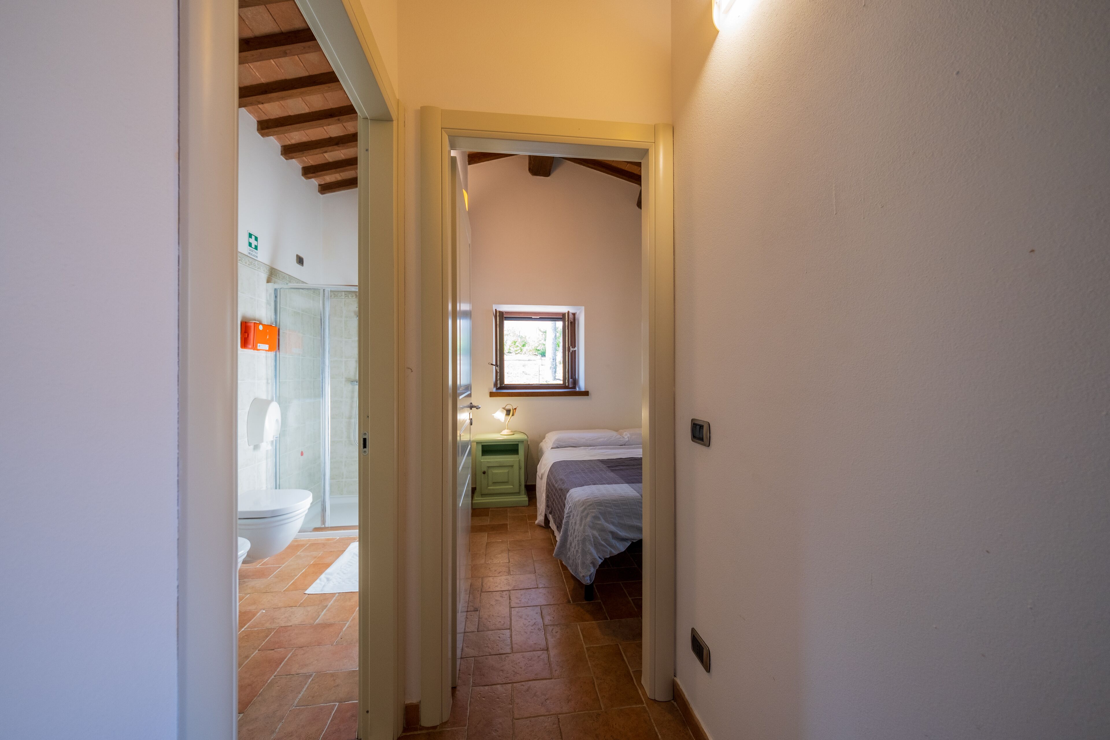 Un couloir étroit mène à une chambre à coucher qui contient un lit, une table de chevet et une fenêtre.