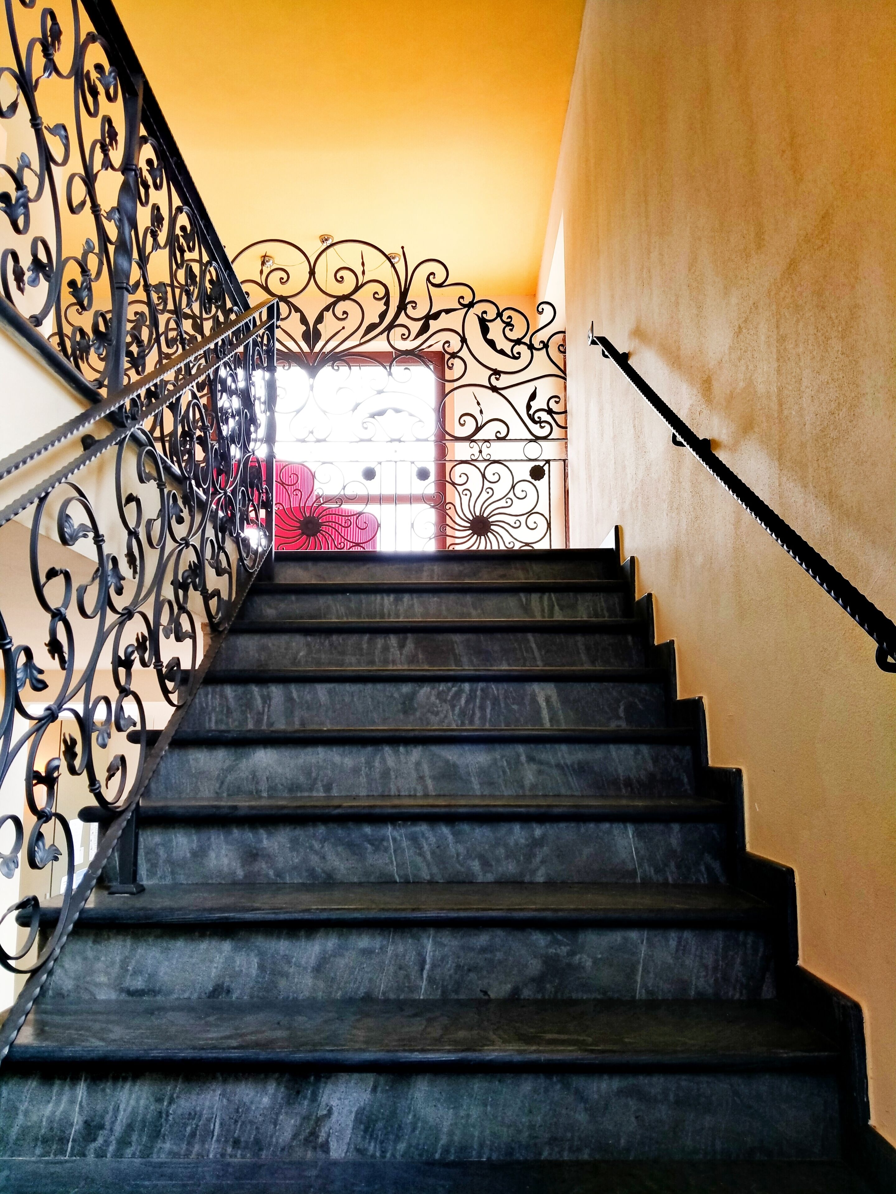 A staircase with ornate black metal railings and a view of a room with a pink bedspread.