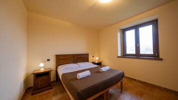 A bedroom with a bed, two bedside tables, a window, and a nightstand with a lamp.