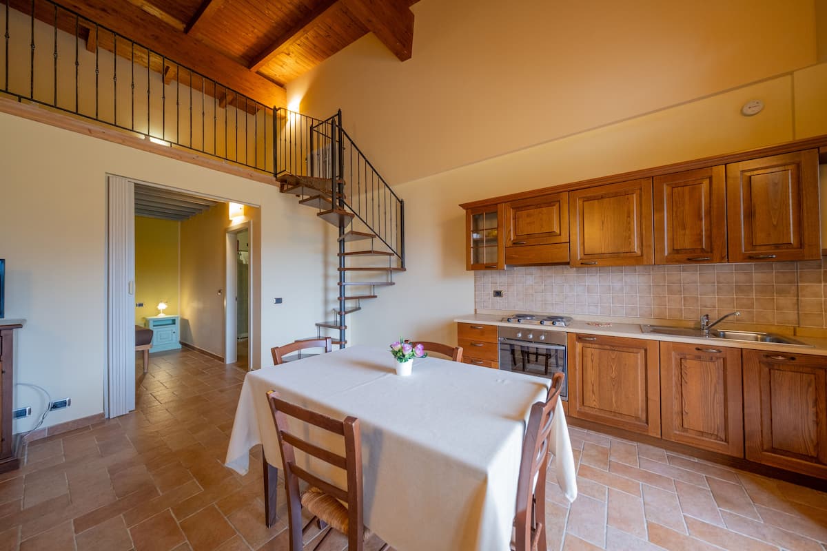 Una cocina con armarios de madera, una mesa de comedor con sillas y una escalera que sube a un nivel superior.