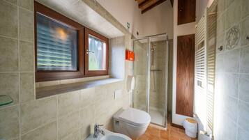 A bathroom with a glass shower enclosure, a toilet, a bidet, and a sink.