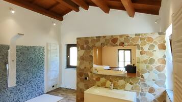 A spacious bathroom with a stone wall, wooden ceiling beams, and a large sink.