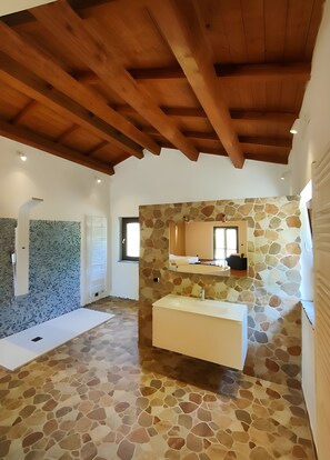 A spacious bathroom with a stone wall, wooden ceiling beams, and a large sink.
