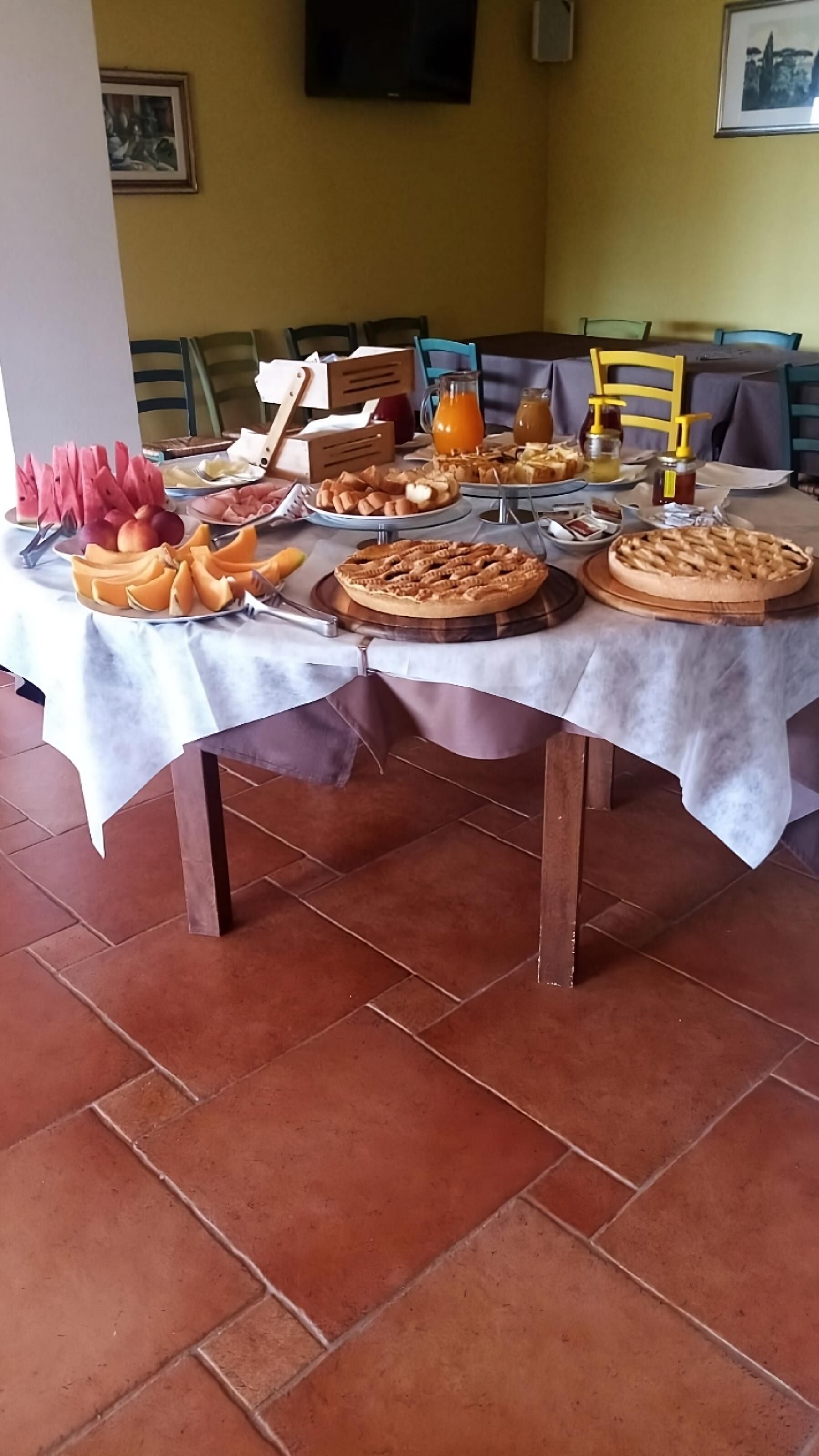 Buffet de café da manhã com diversos alimentos e bebidas sobre uma mesa coberta com toalha branca.
