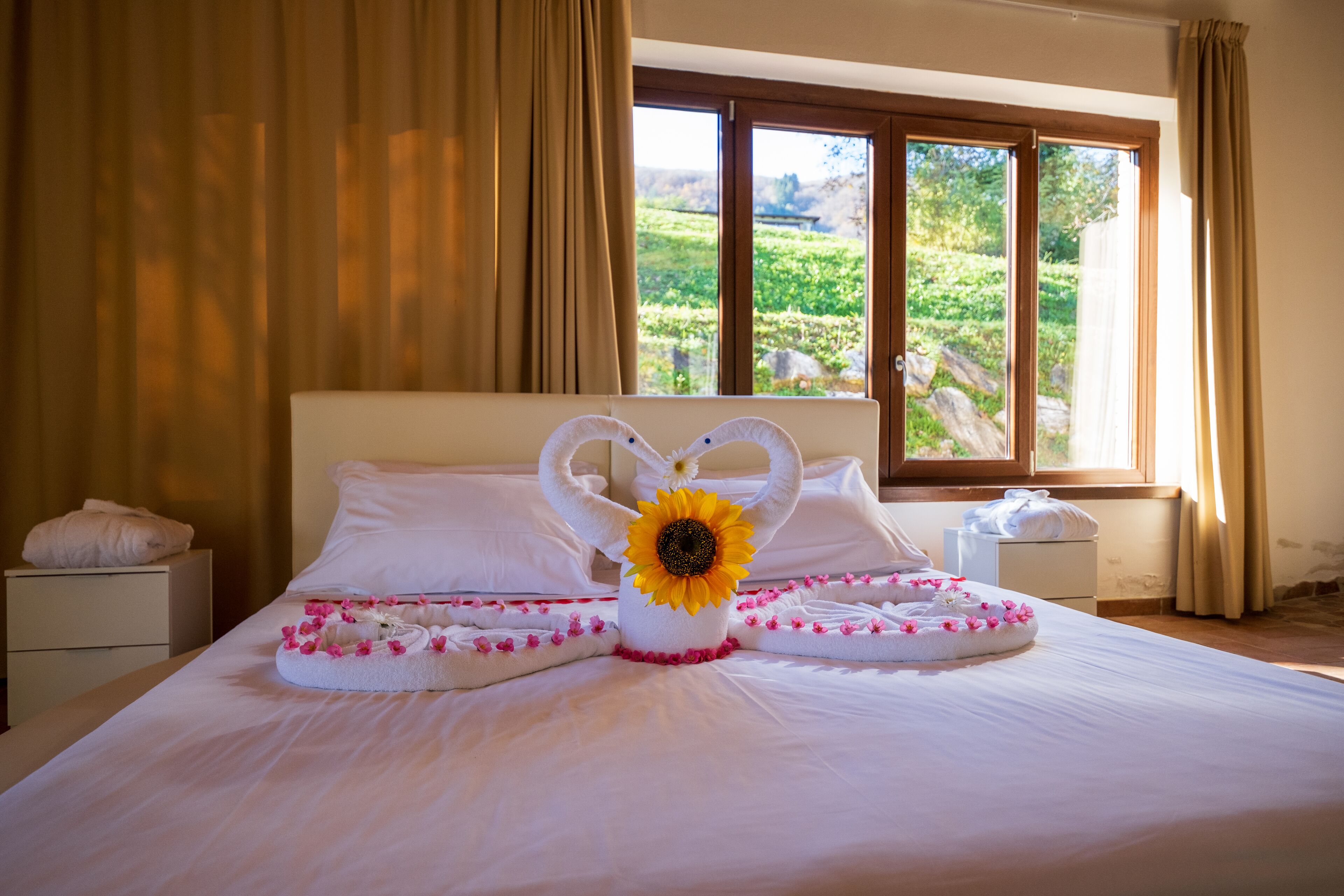 A neatly made bed with white linens, a heart-shaped towel arrangement, and a sunflower centerpiece.